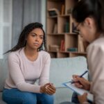 Therapist taking notes as a client shares what she is going through in a therapy session